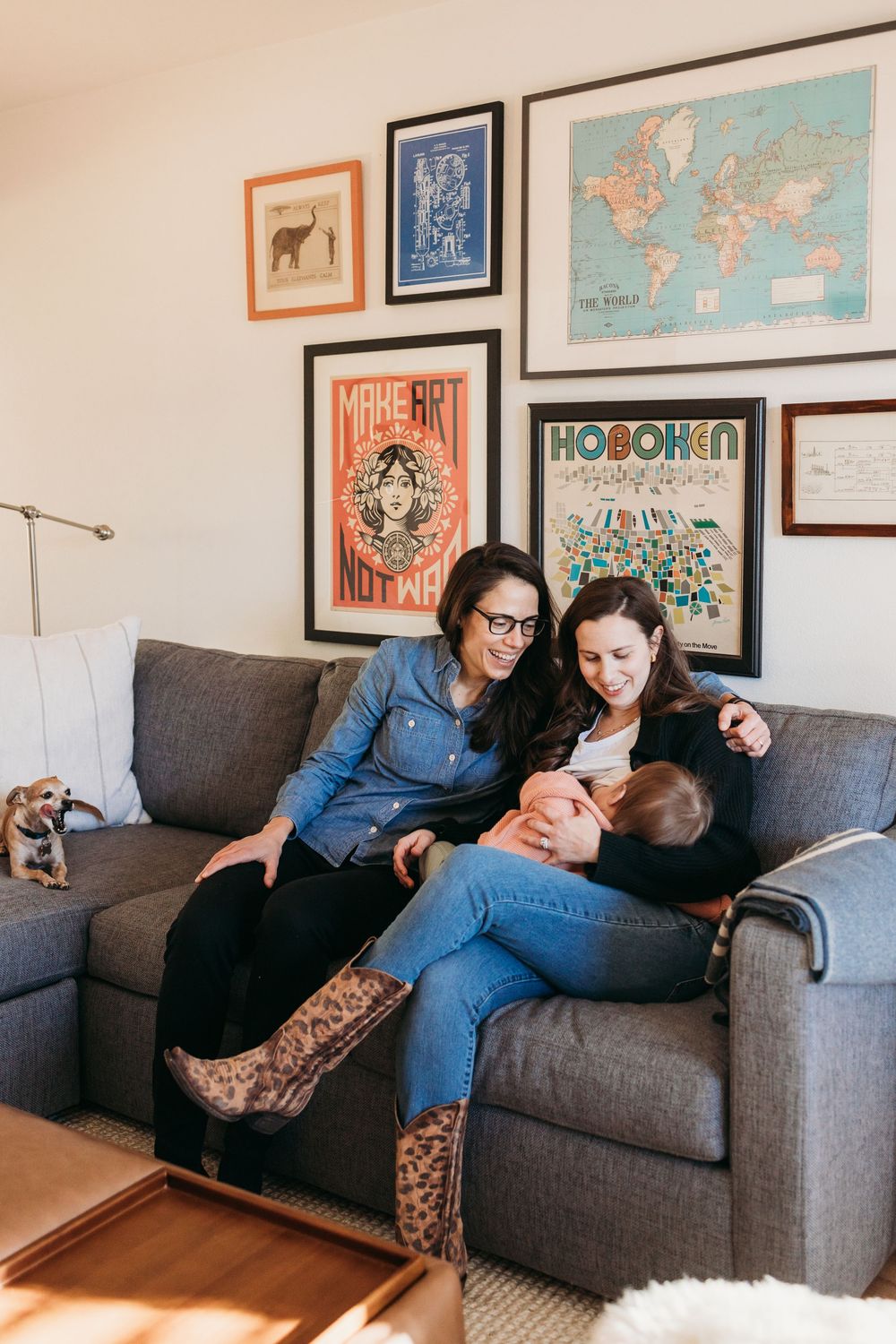 Family relaxes together on grey couch in living room with decorative wall art featuring maps and posters.