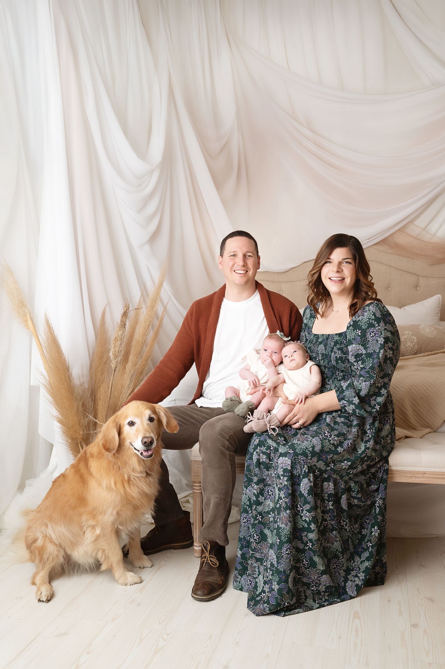 Studio family portrait with twin babies and golden retriever on cream backdrop.