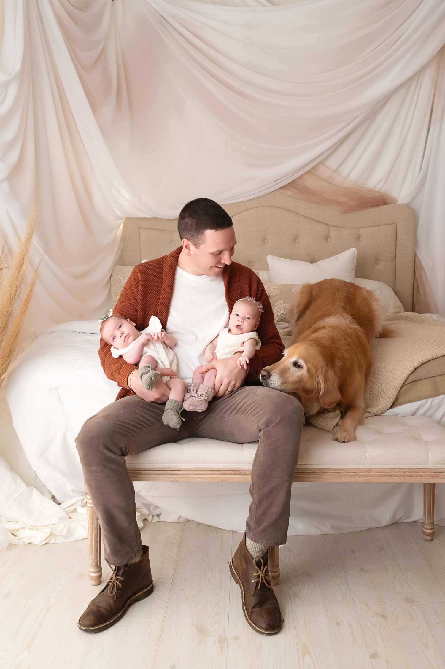 Parent on bench with twin babies and golden retriever in studio setting.