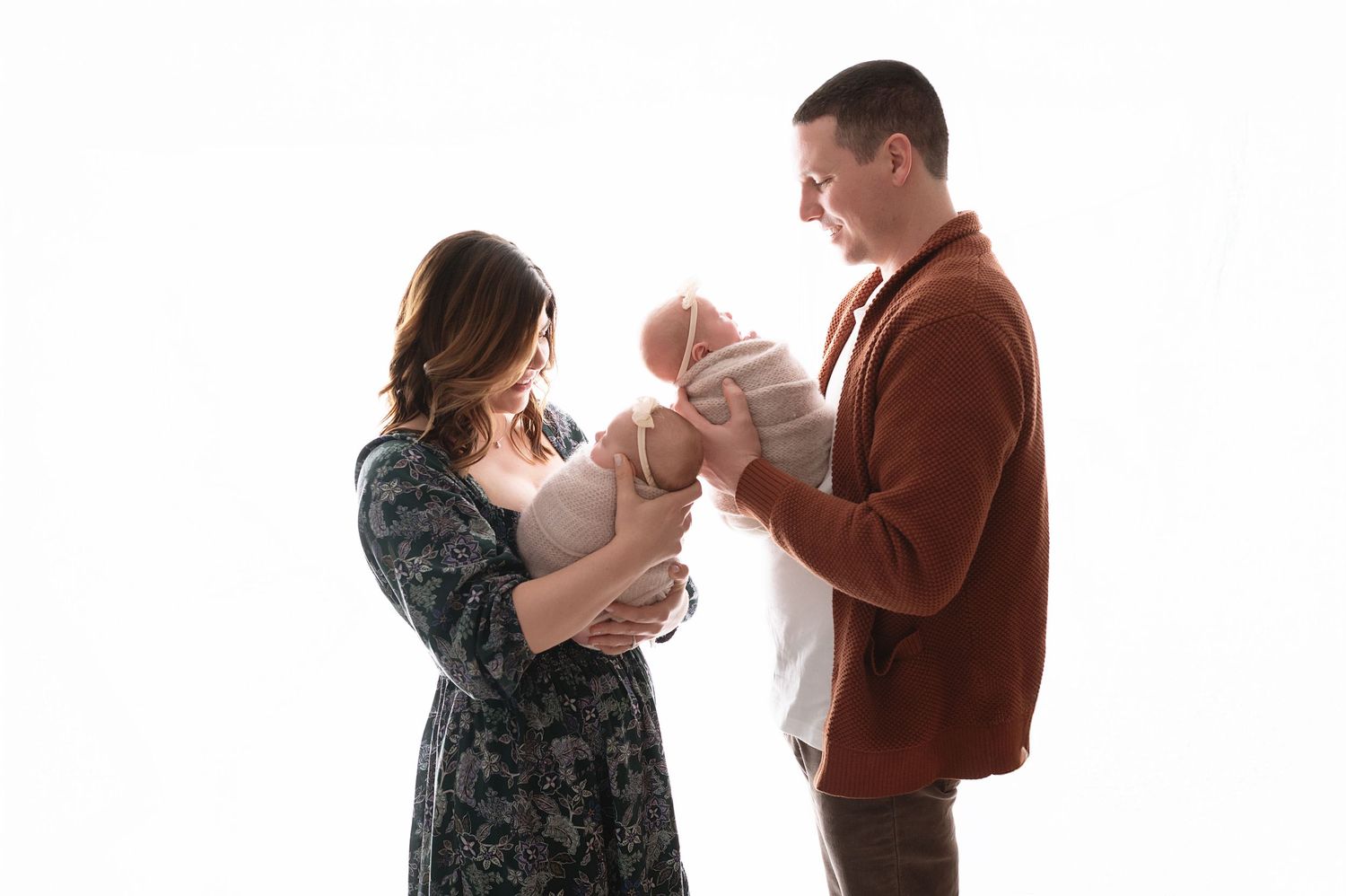 Parents in casual attire holding twin babies against white backdrop.
