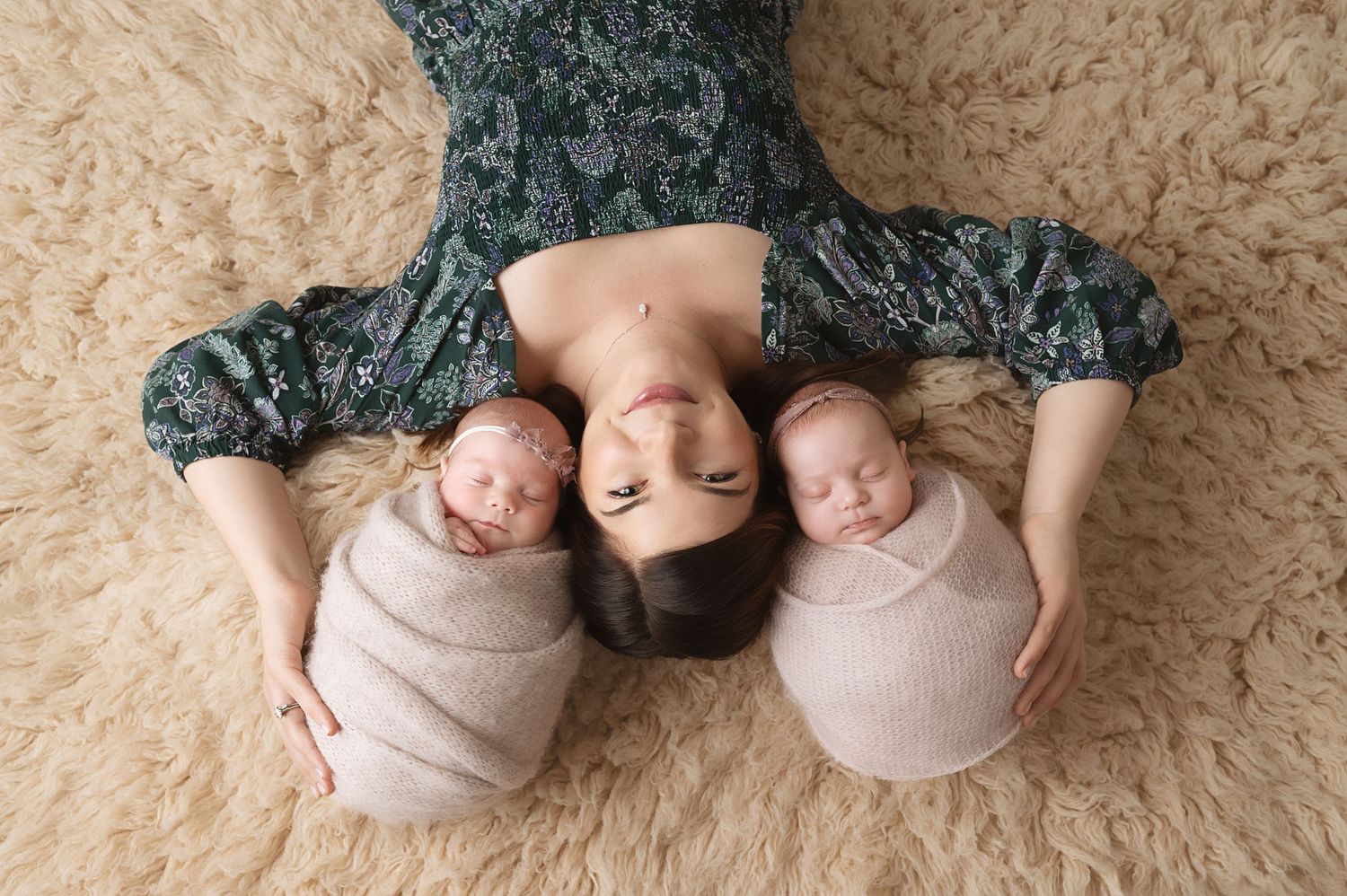 Sleeping twin newborns wrapped in beige blankets on plush carpet.