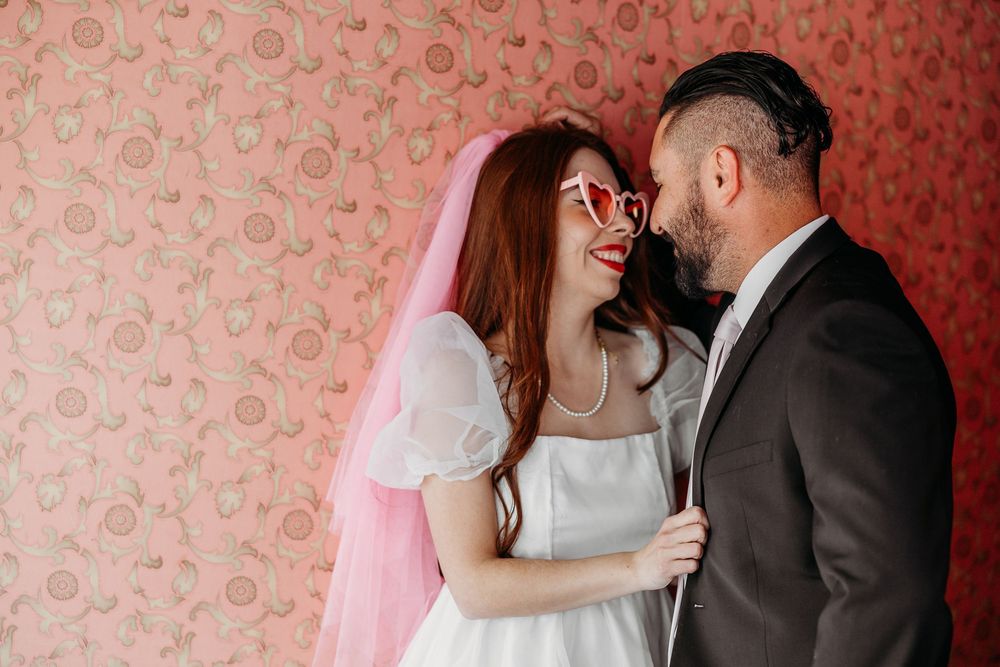 A joyful couple shares an intimate moment against a pink floral wallpaper backdrop.