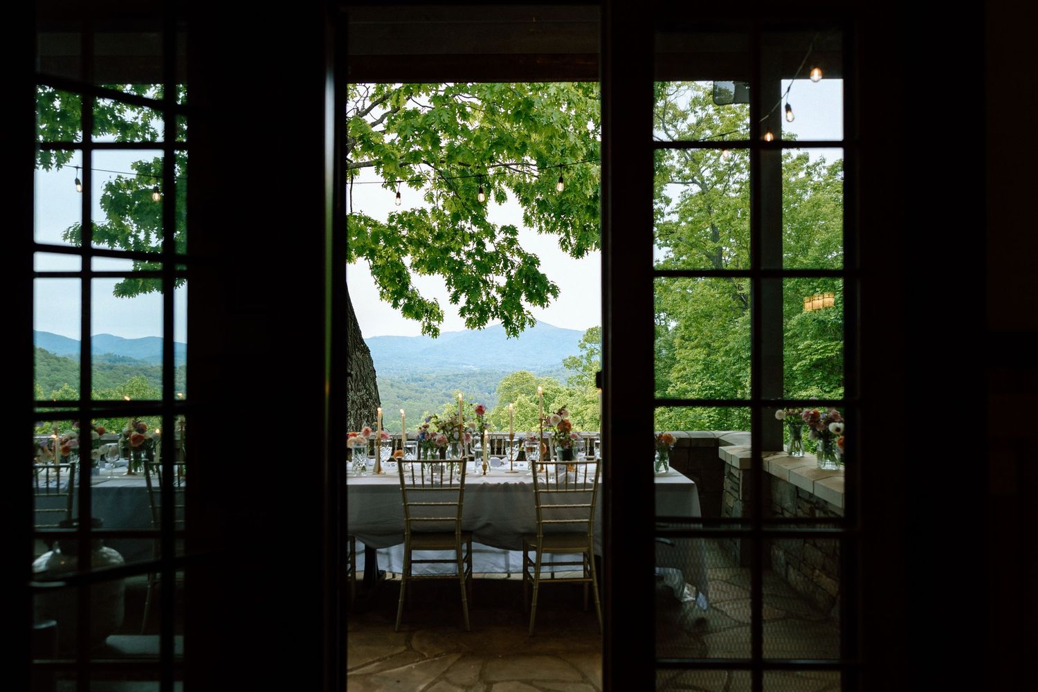 Window view from inside the Grand Eagle airbnb in Asheville, looking out to a terrace with chairs and mountain vistas through tree leaves.
