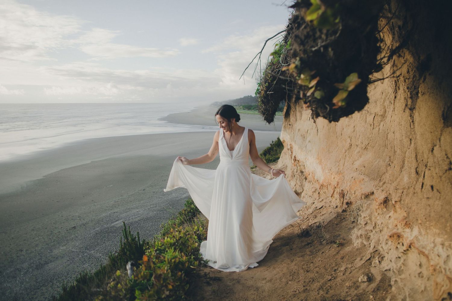 Figure in flowing white dress stands on dramatic coastal cliffside overlooking ocean vista.
