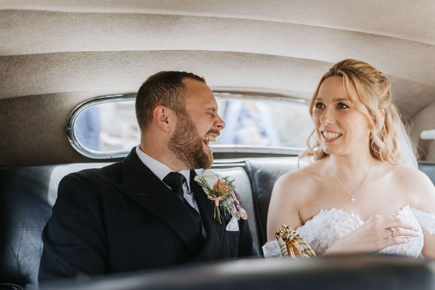 Two newlyweds share a joyful moment while sitting together in the back of a vintage car.