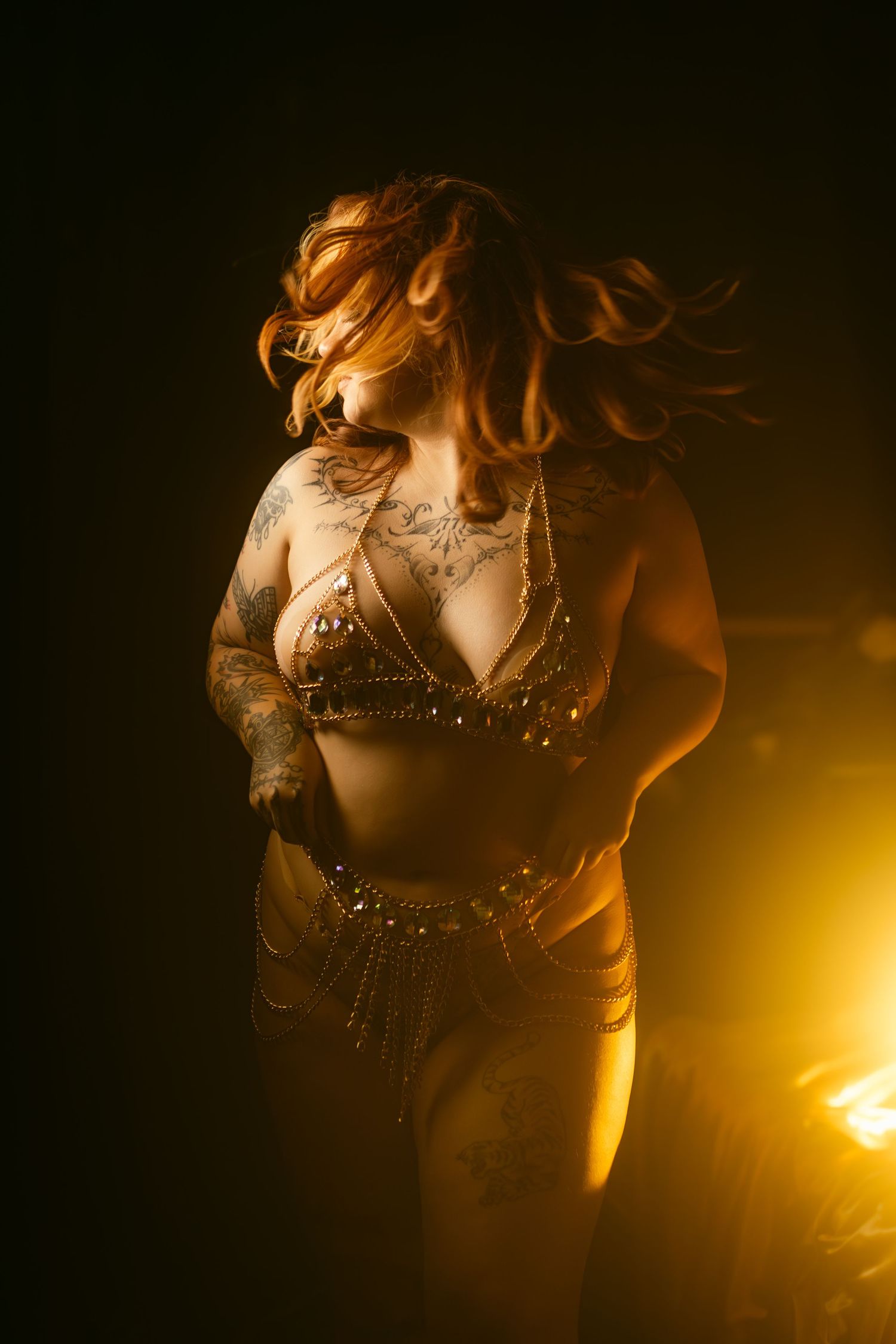 Fort Worth boudoir photo against dark background with dramatic golden backlighting and pin-like light streaks showing floral tattoo artwork.