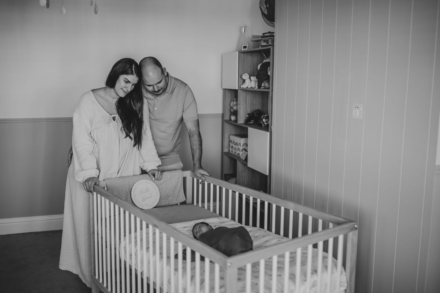 Two adults looking down into a white wooden crib while setting up a nursery in a monochrome photograph.