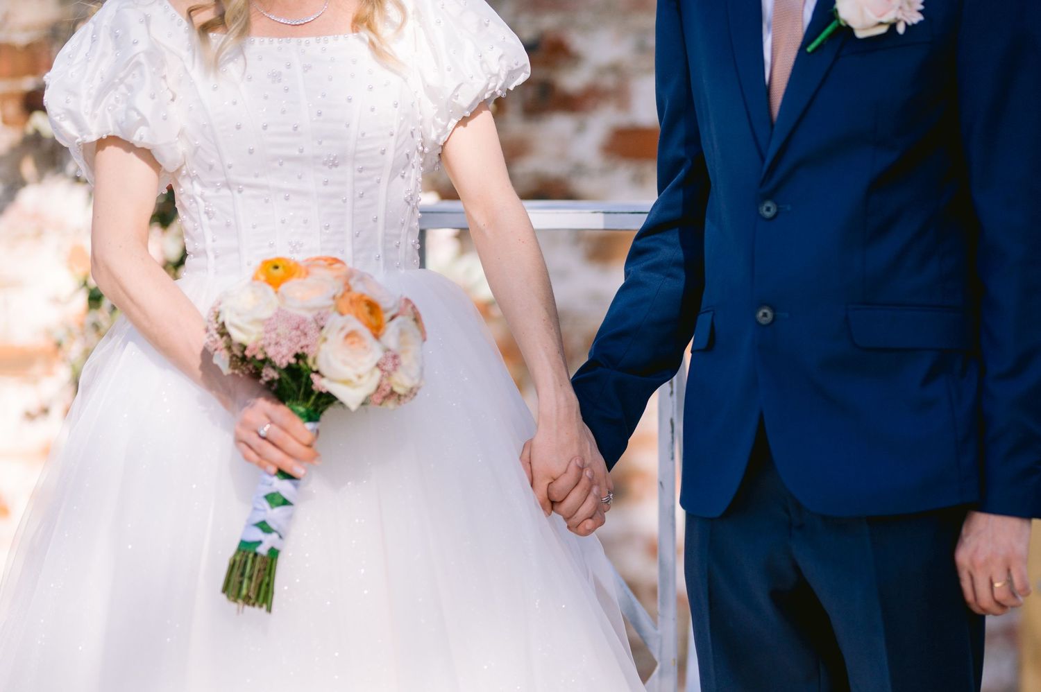 Close up of wedding couple holding hands with bridal bouquet of peach roses.