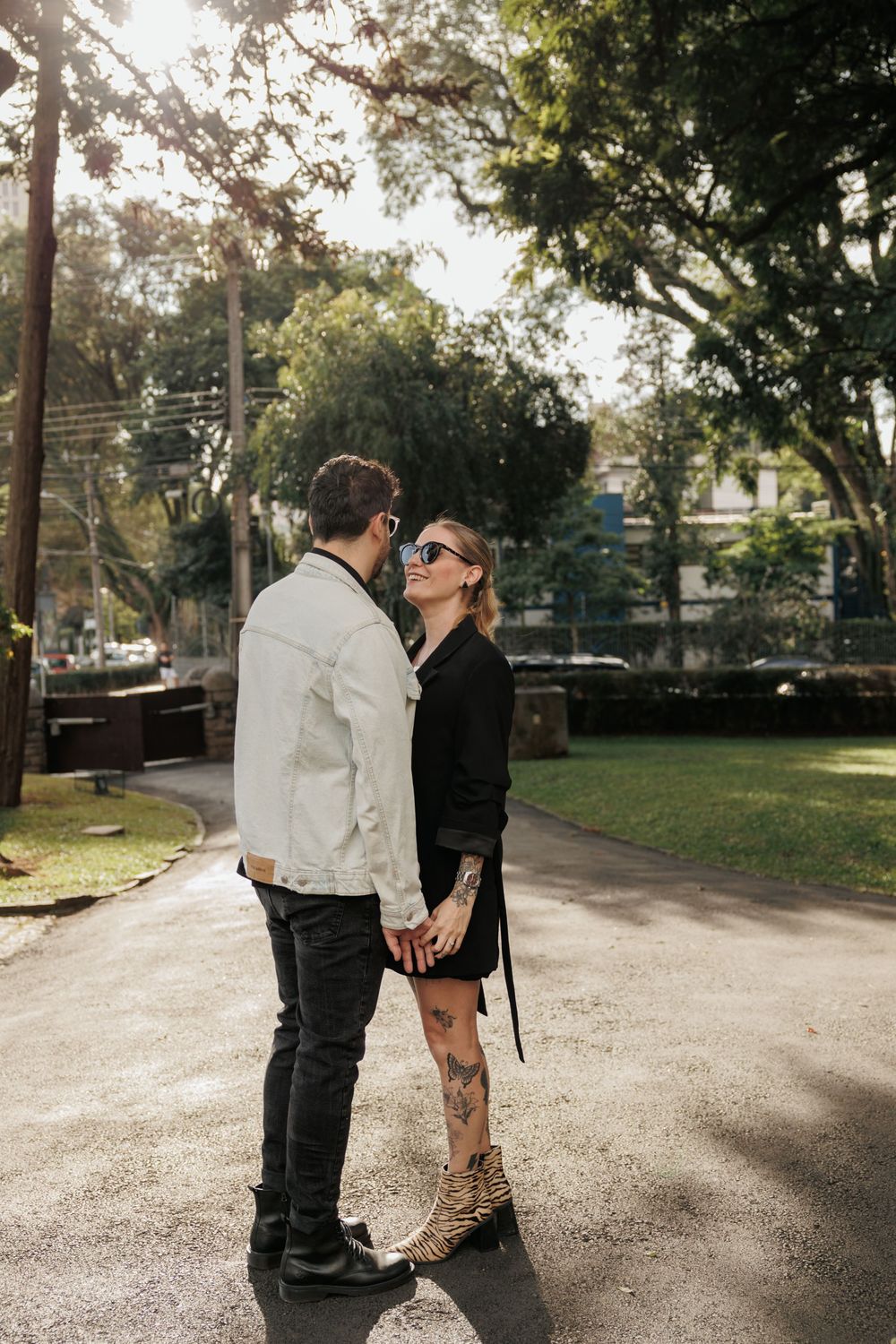 A couple shares an intimate moment on a tree-lined path in a park on a sunny afternoon.
