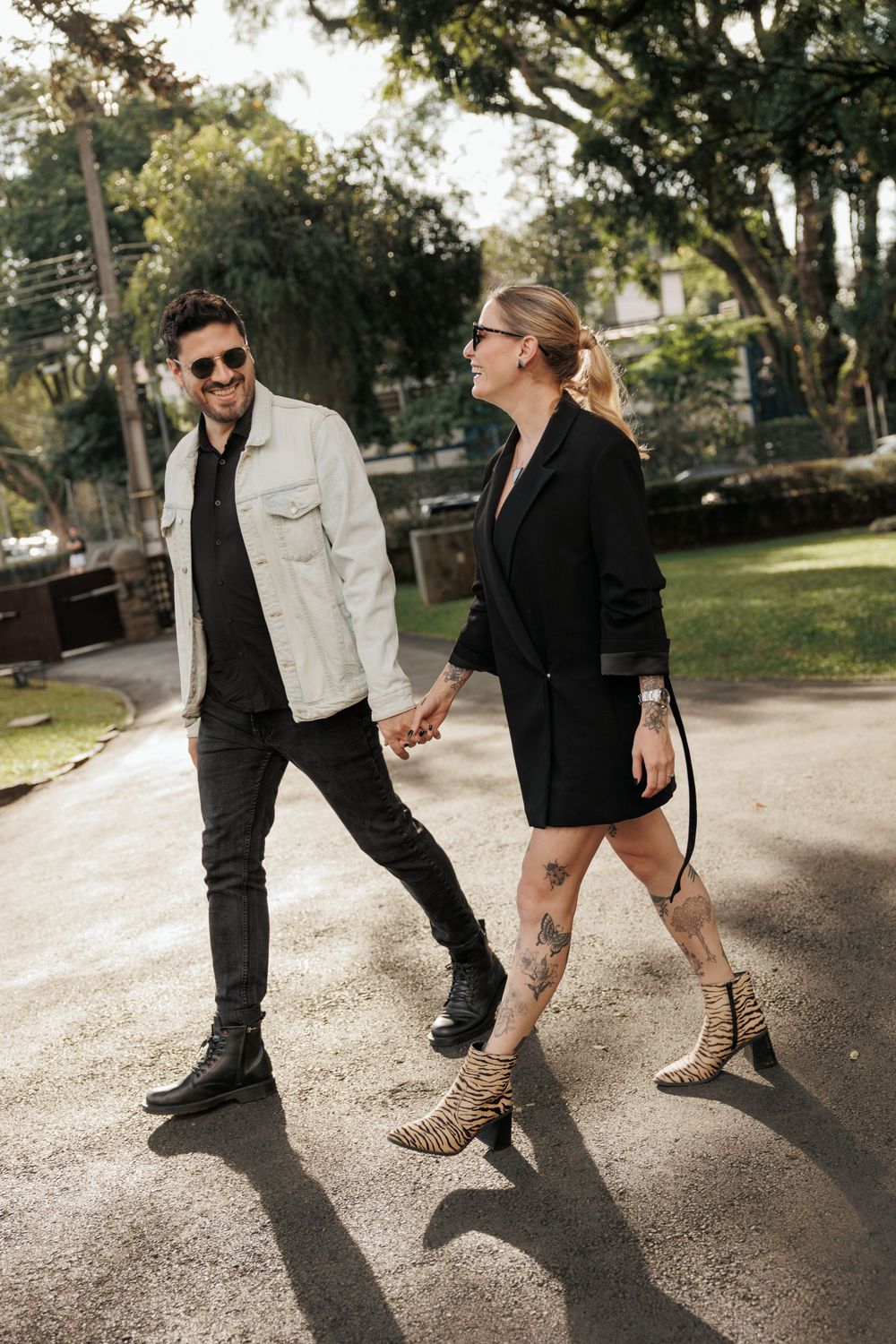 Stylishly dressed couple walking together on a path through a sunlit park wearing contrasting black and white outfits.