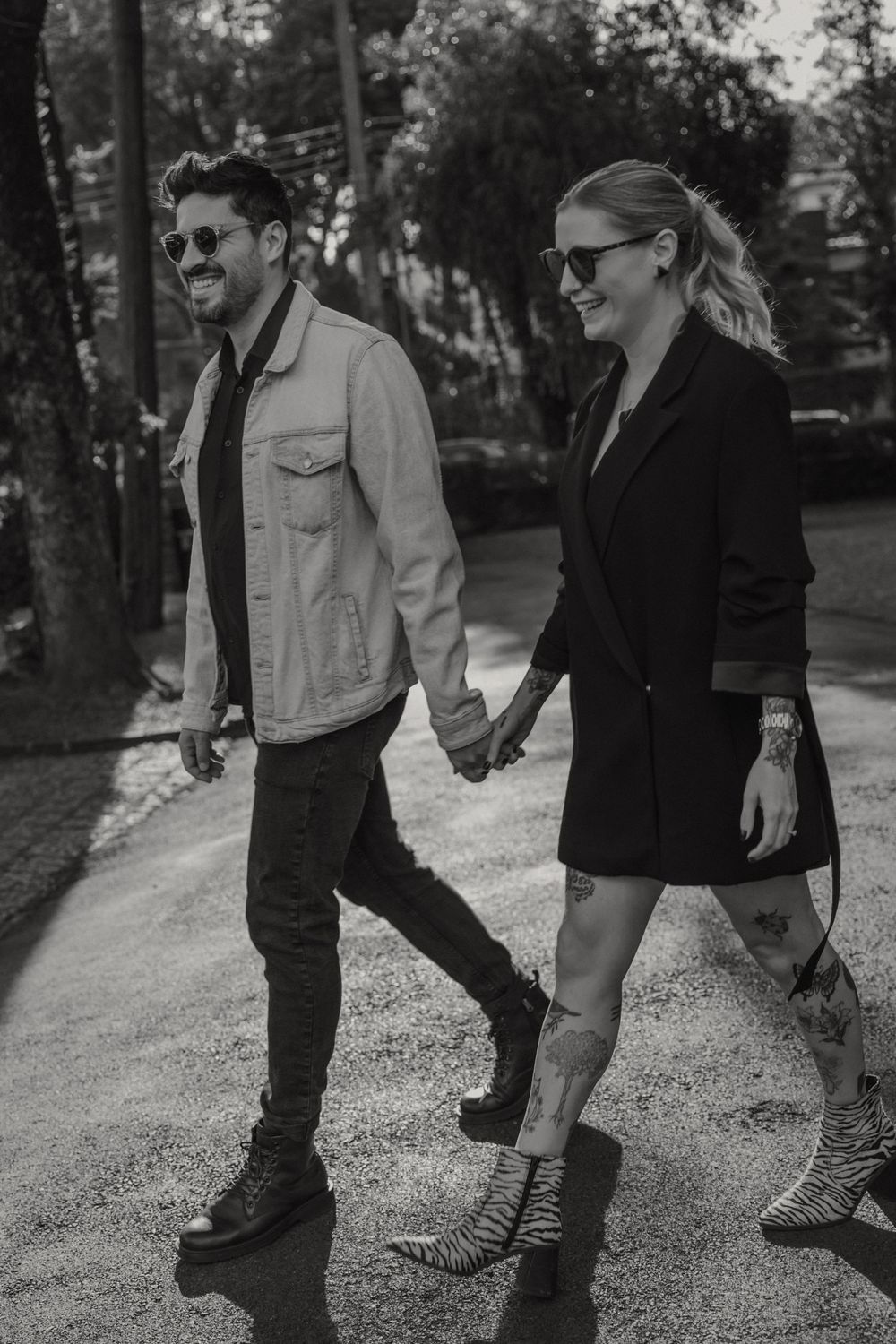 A stylish couple holding hands while walking outdoors in black and white, wearing sunglasses and casual fashion attire.
