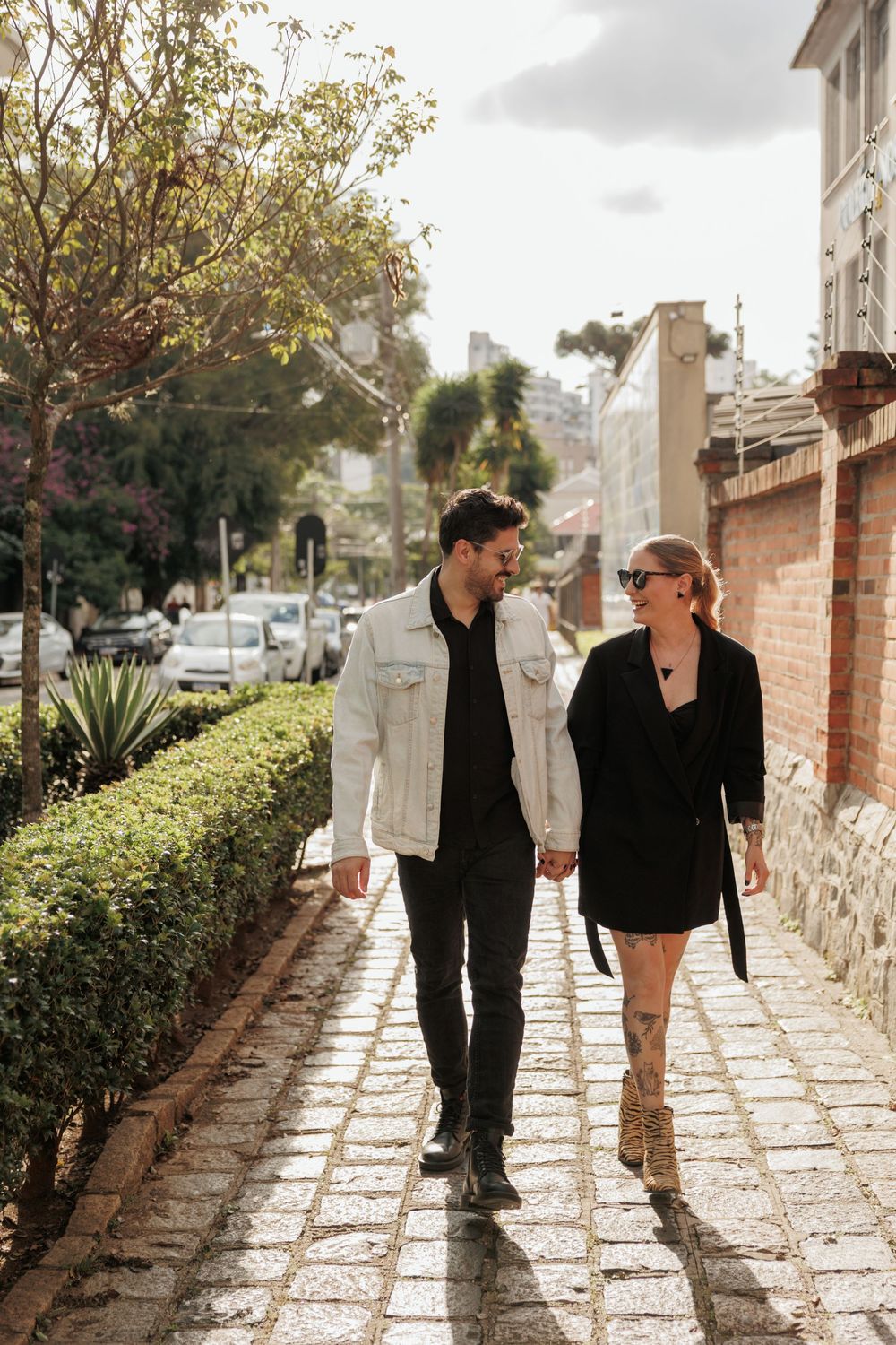 A couple holding hands while walking together on a cobblestone sidewalk along a Mediterranean street on a sunny day.