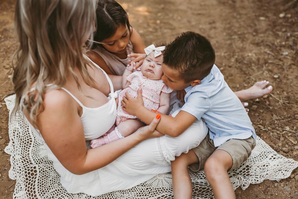 Family sharing tender moment together with newborn baby outdoors on blanket in natural setting.