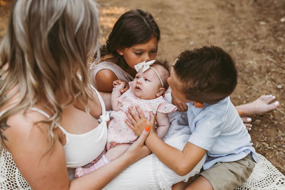 Tender family moment outdoors with small baby and children in white and blue clothing.