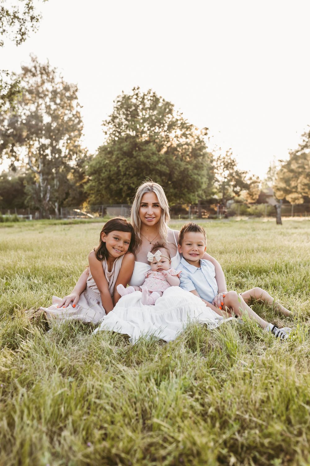 Family lying together in grassy field during golden hour wearing coordinated white outfits.