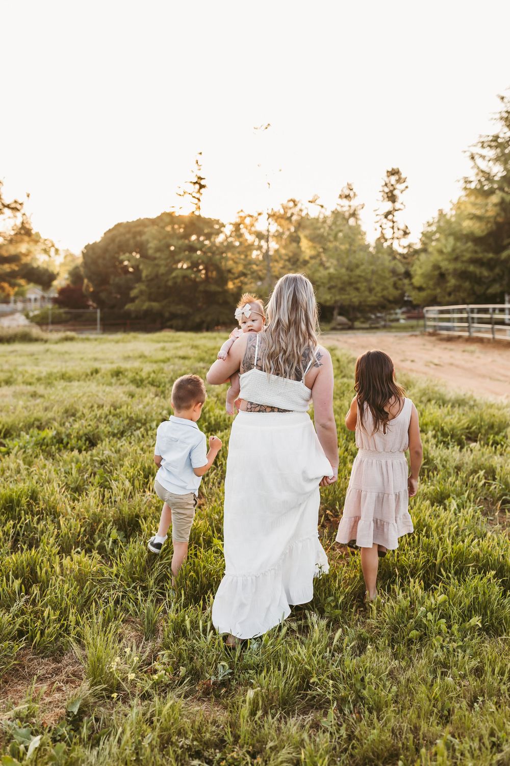 Family walking together in a sunlit meadow with white fencing and trees at sunset.