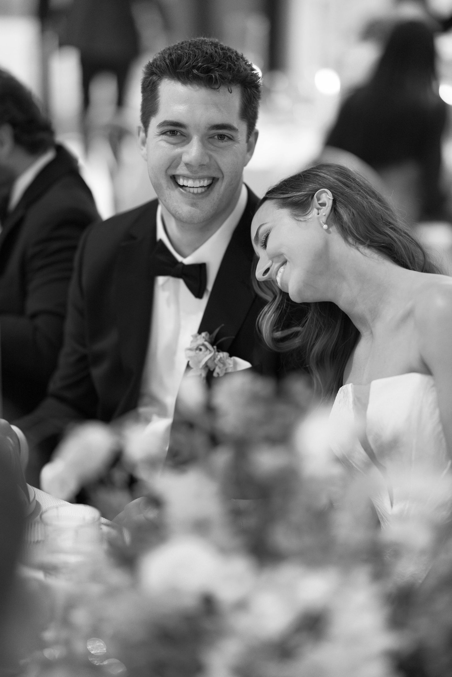 Black and white candid wedding reception photo showing joyful couple seated at decorated table.