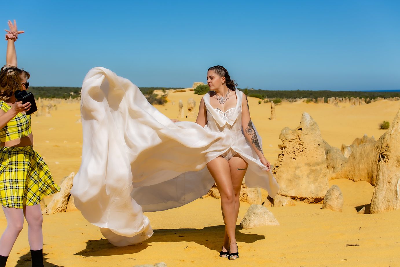 Dancing figures in flowing white dresses create a dynamic scene against a golden sandy beach landscape.
