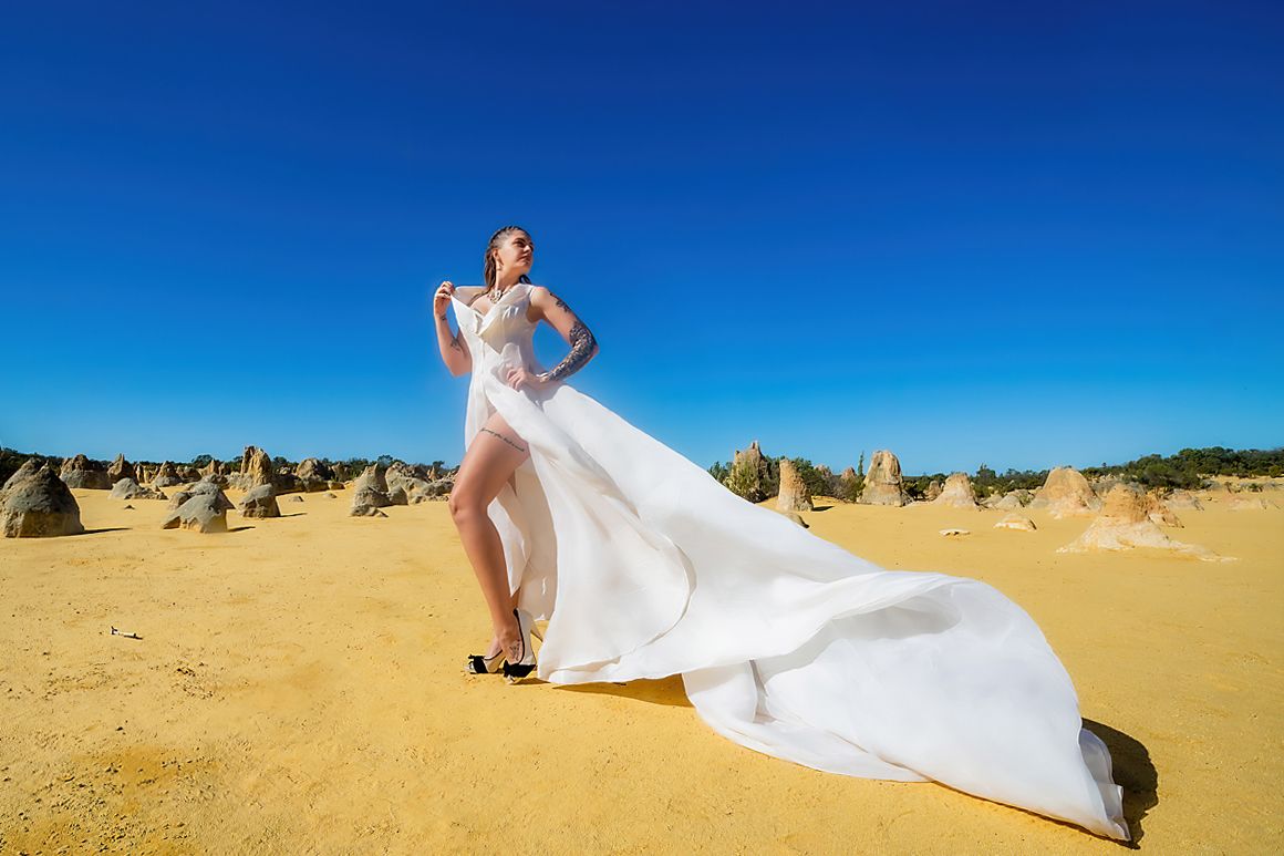 Flowing white dress billowing dramatically against desert landscape with limestone formations at Pinnacles Desert in Australia.