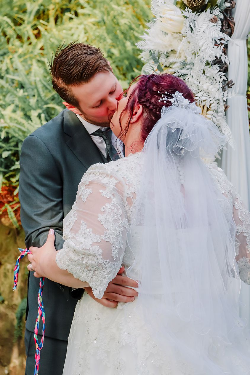 A romantic wedding moment captured outdoors with the bride's lace dress and flowing veil against a natural garden backdrop.