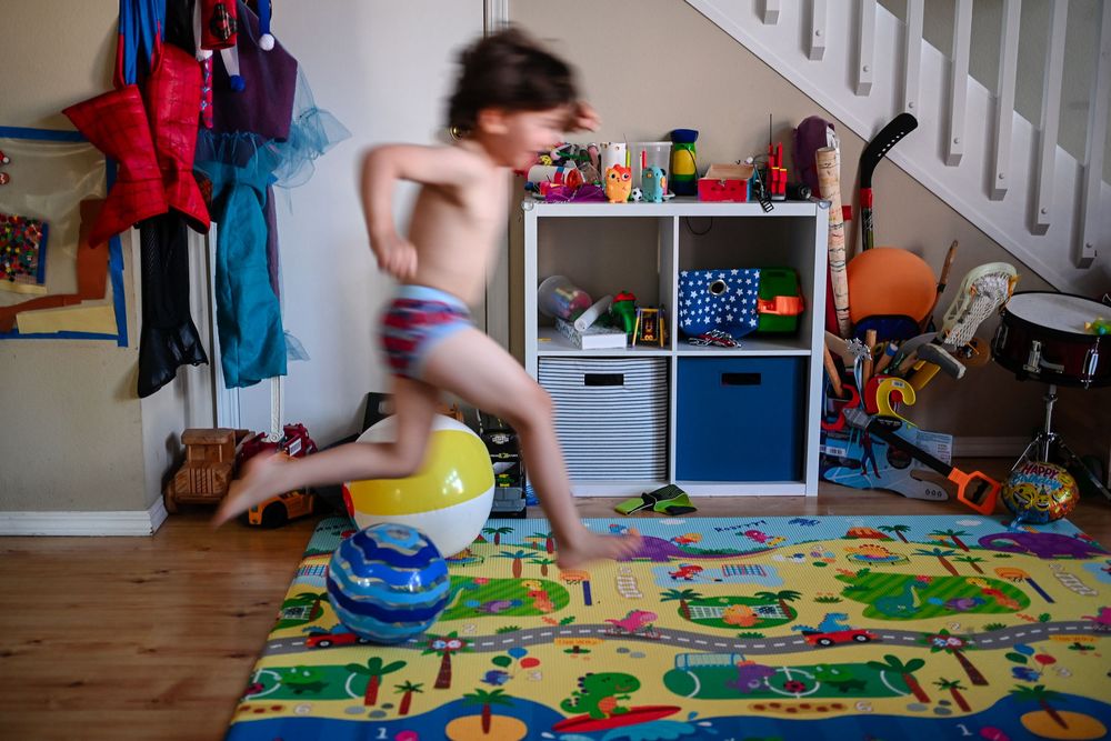 Child jumps and plays energetically in colorful playroom with toys and activity mat on hardwood floor.