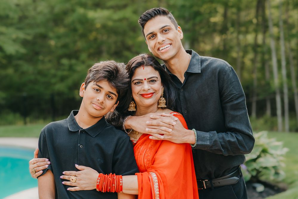 A mother and her two sons wearing red and black outfits pose affectionately for outdoor family photos in a wooded setting.