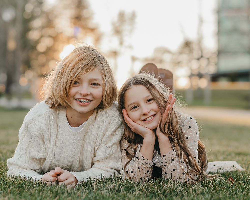 Two siblings lying together on grass enjoying each others company in multiple candid outdoor portraits.