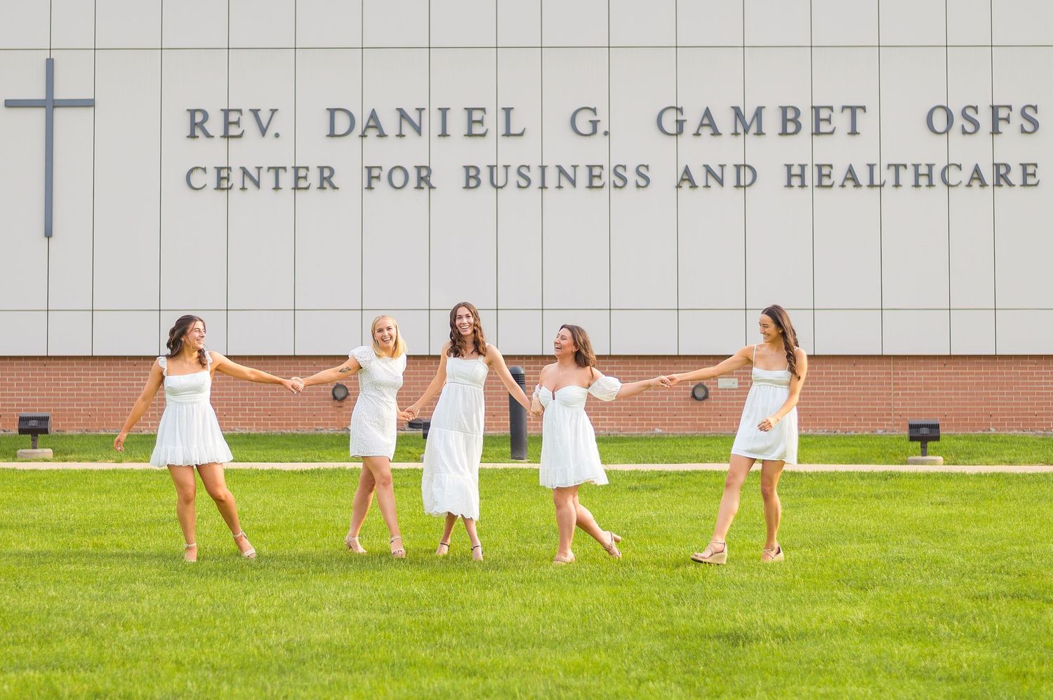 Group in white dresses dancing joyfully on grass in front of a business center building.