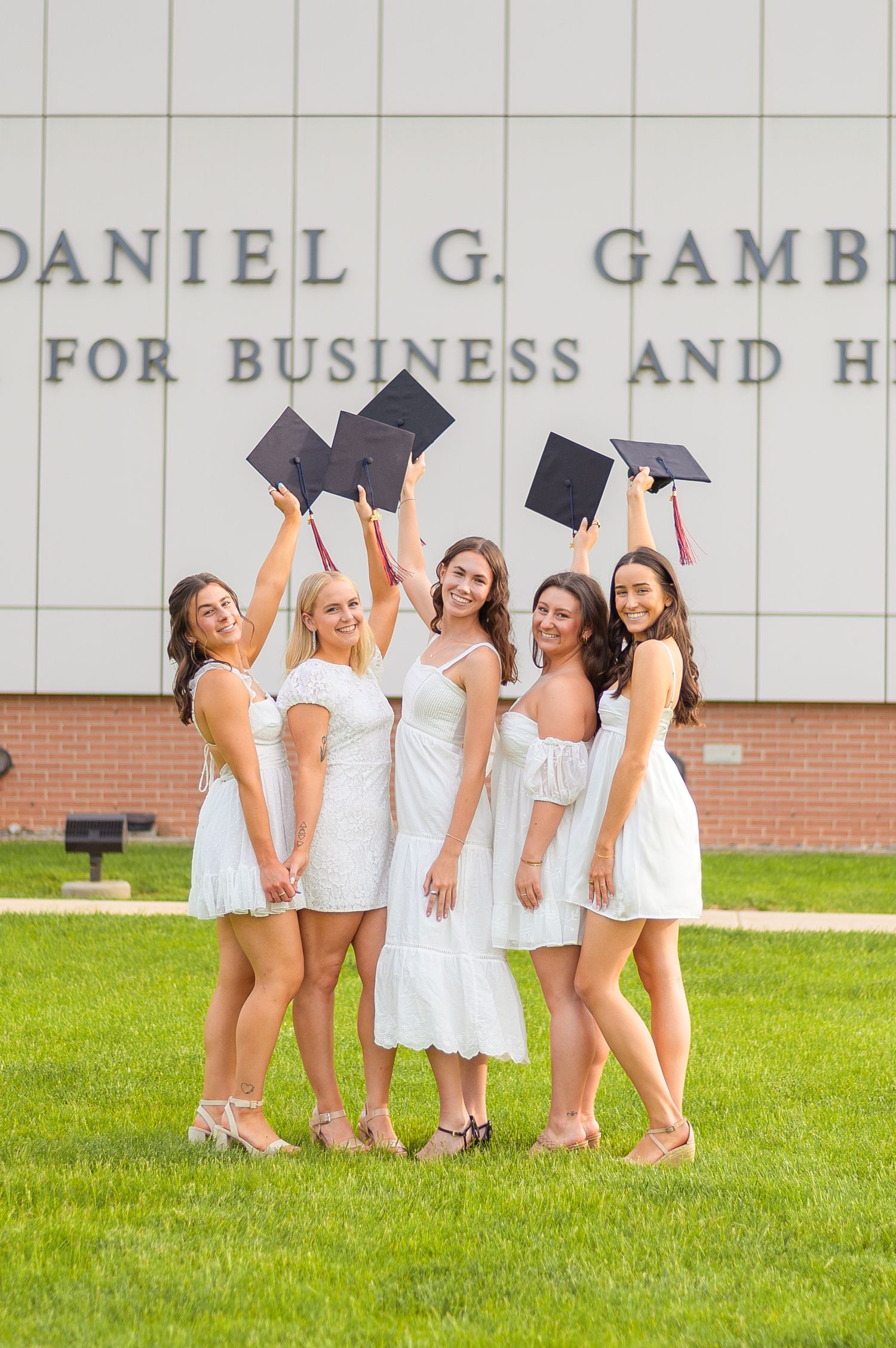Graduates toss their caps while celebrating in front of campus building.