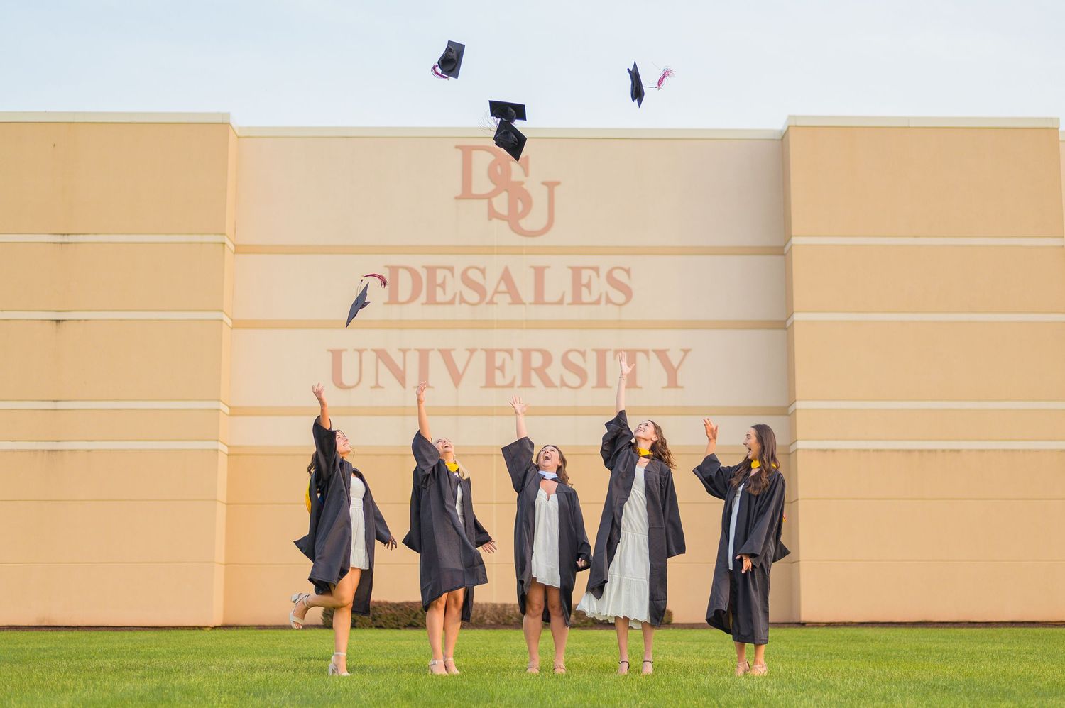 Graduates throwing caps in the air against beige university wall background.