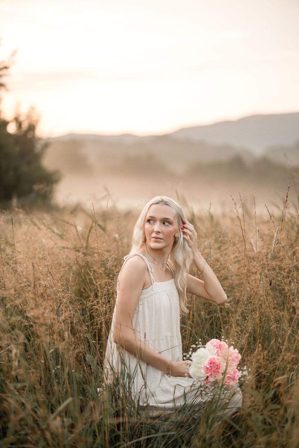 A dreamy golden hour portrait in a meadow featuring a white summer dress and pink flowers.