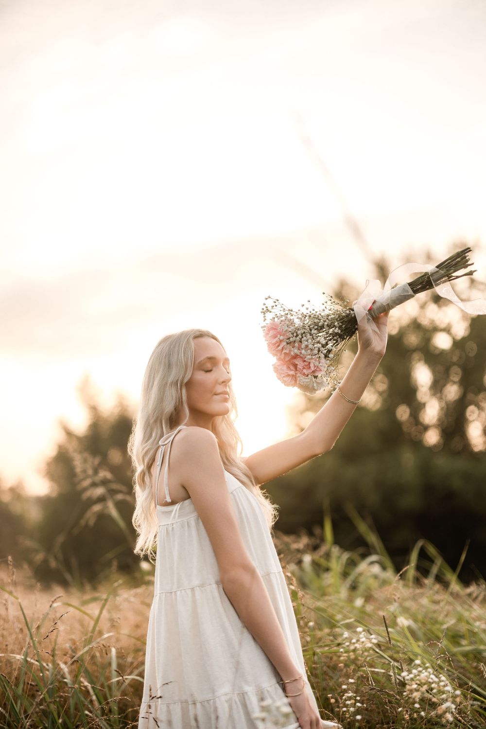 White dress flowing in golden meadow with wildflowers at sunset.