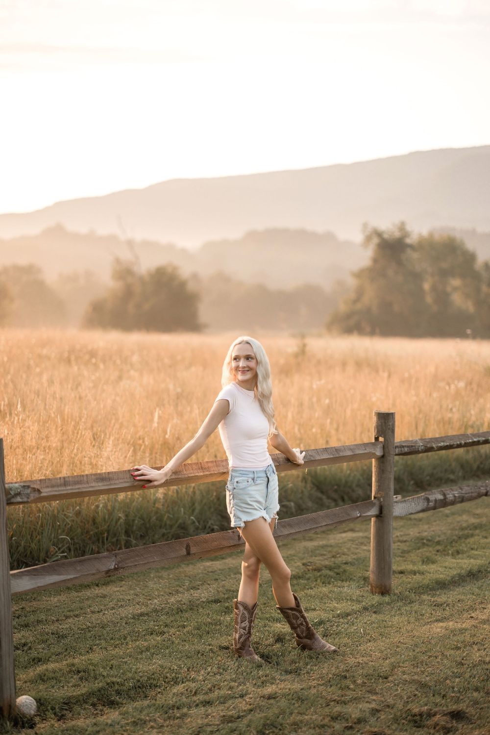 A summer portrait in a golden field with mountains in the background features a casual country-inspired western style outfit.