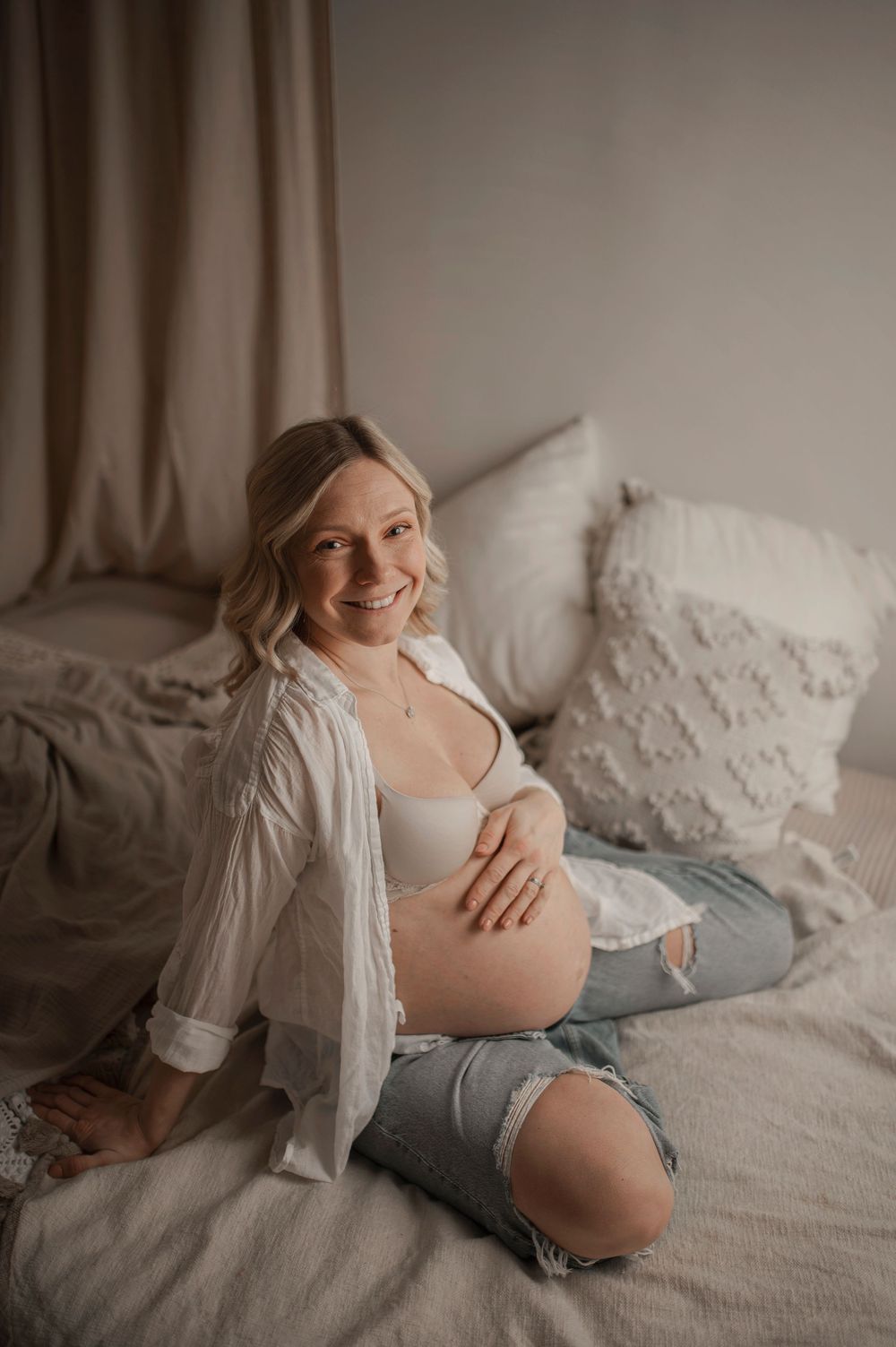 Light and airy maternity photo sequence showing an expectant mother relaxing on white bedding while wearing a white shirt.