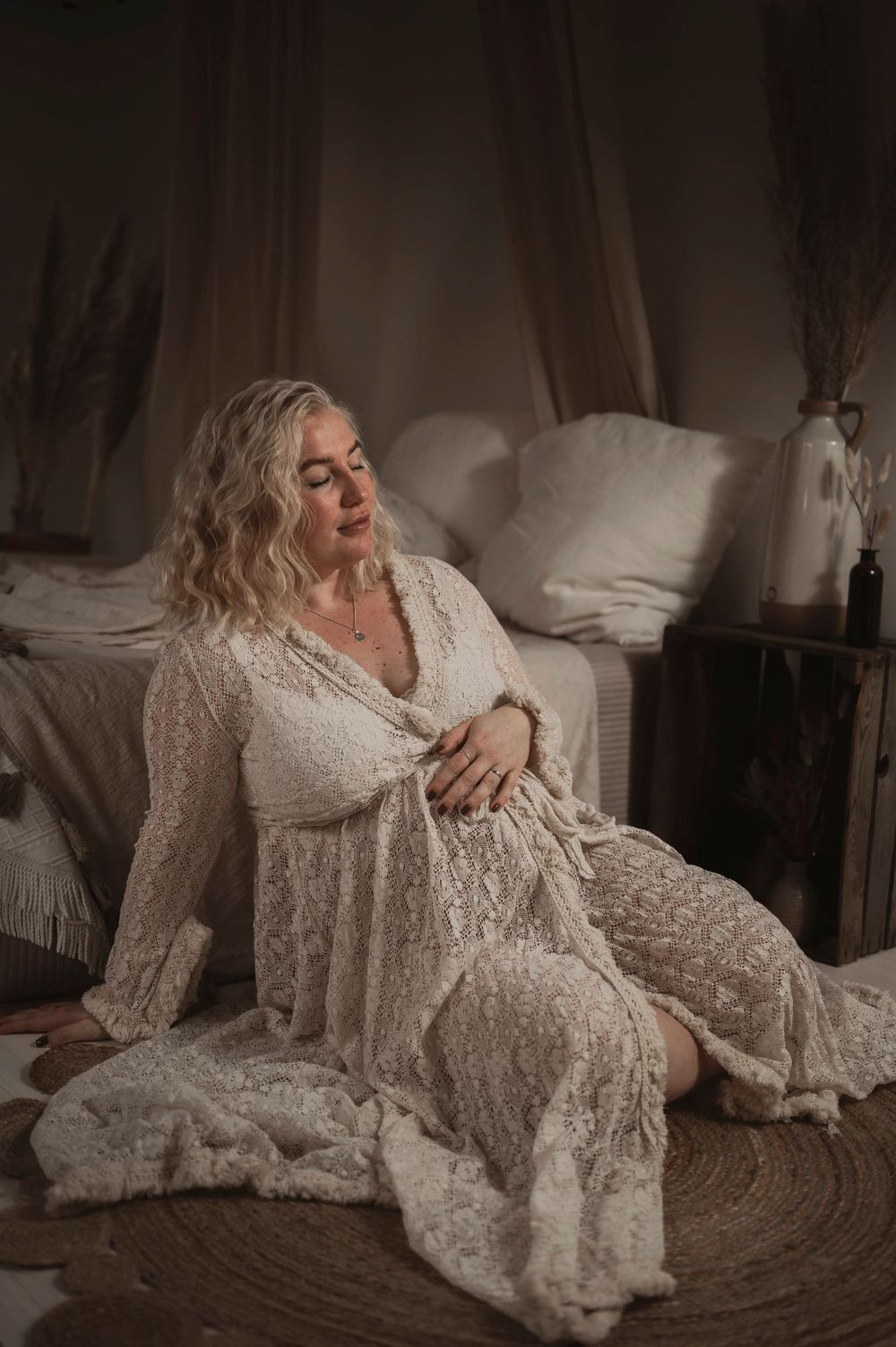 A person reclining on cushions wearing a vintage white lace dress in a moody boudoir setting.