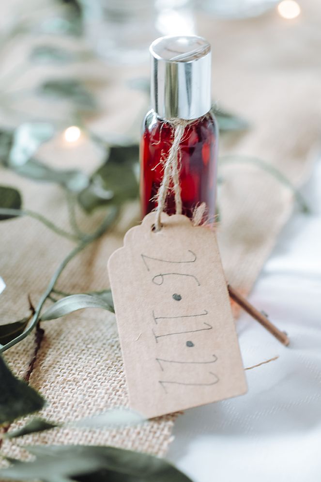 A small red glass bottle with a silver cap and rustic tag sits on burlap fabric with soft bokeh lighting effects.