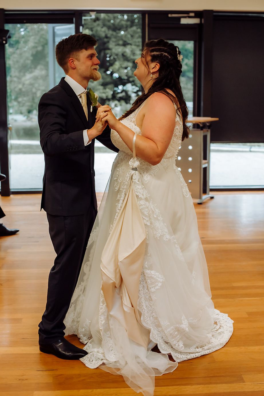 A couple shares their first dance at their wedding reception on a hardwood floor while wearing formal attire.