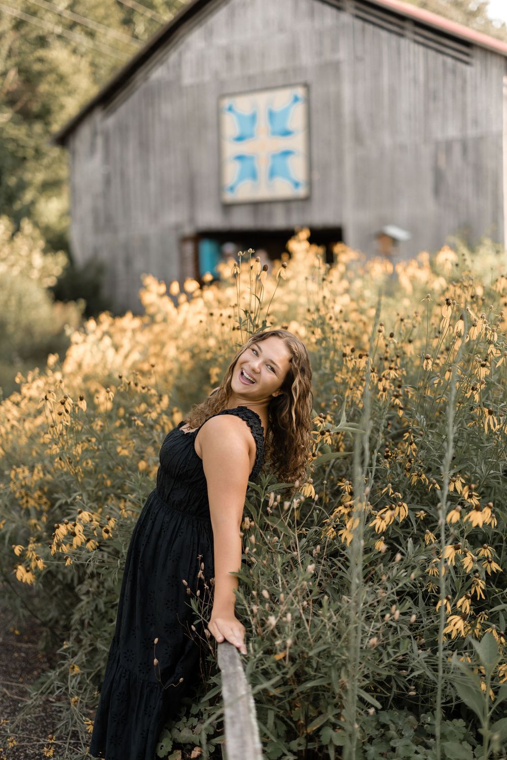 Rustic wooden barn with teal accents stands behind a flowering wildflower meadow at golden hour.