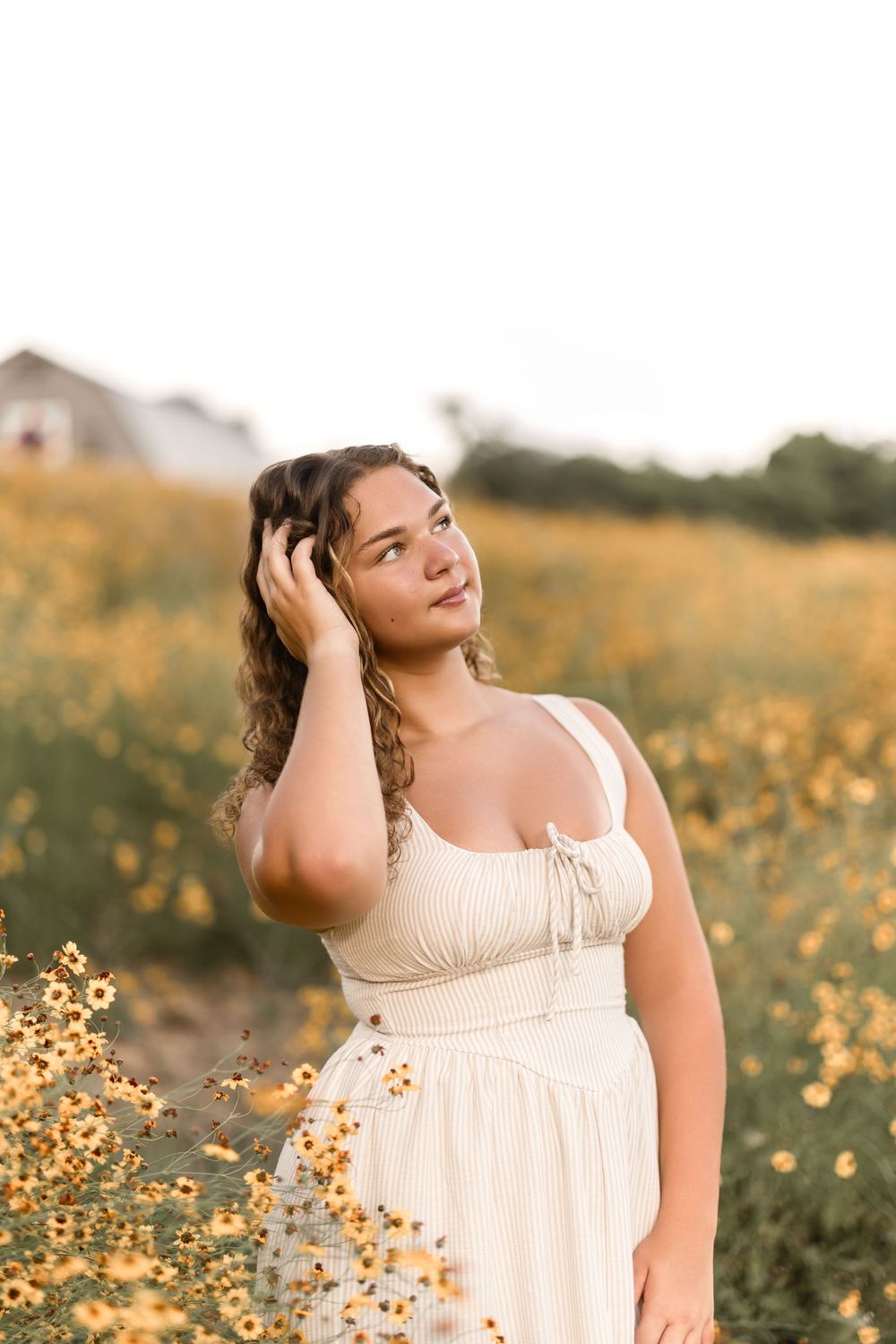 A person in a cream-colored dress poses in a field of yellow wildflowers during golden hour.