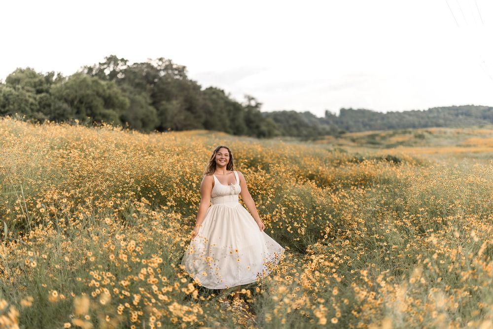 Person in a flowy white dress twirls among vibrant yellow wildflowers in a sunlit meadow during golden hour.