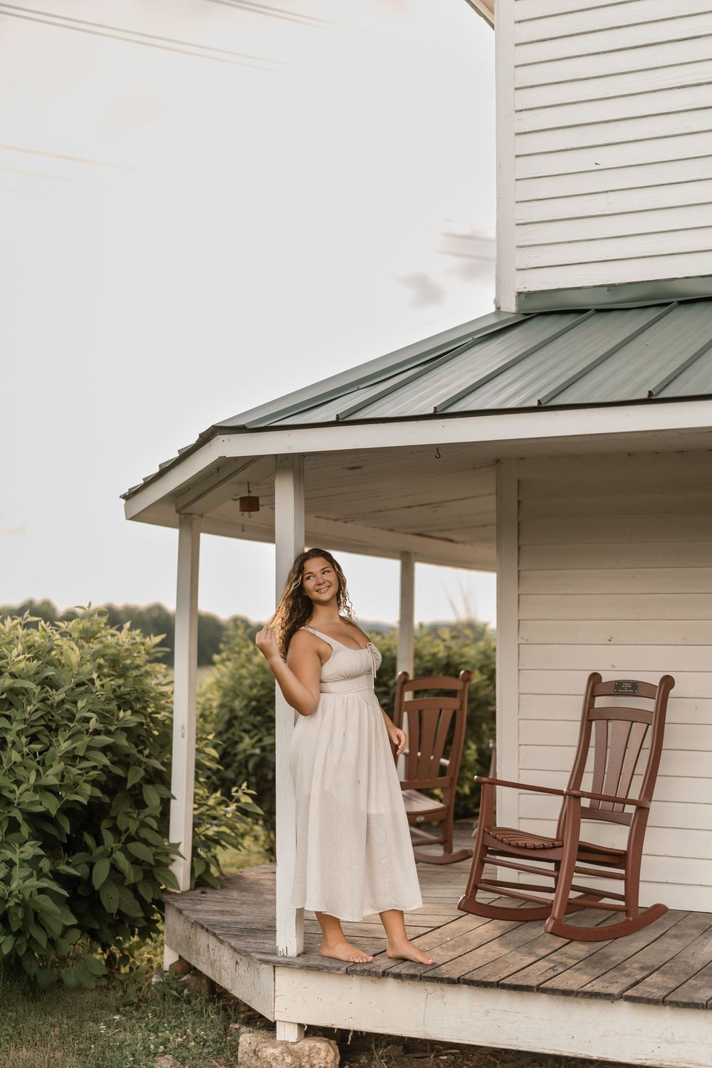 A white sundress contrasts beautifully against a rustic farmhouse porch with classic wooden rocking chairs.