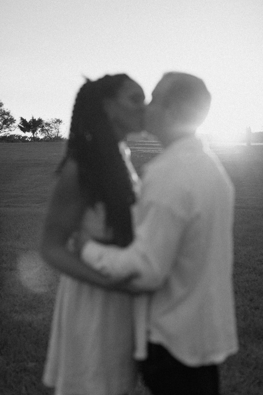A black and white silhouette photo of a couple embracing in a field.