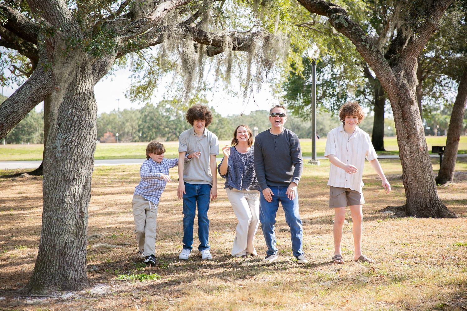 Family members walk together across a tree-lined outdoor setting in coordinating casual outfits.