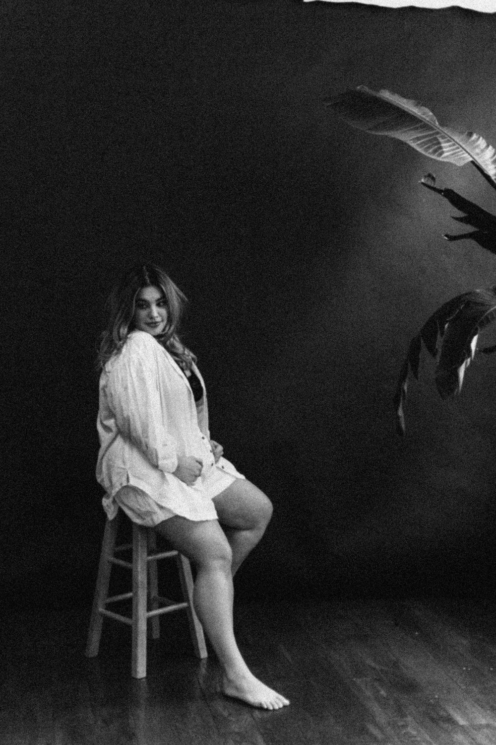 A haunting black and white photo series showing a woman in white crouched on a wooden stool in a dark room.