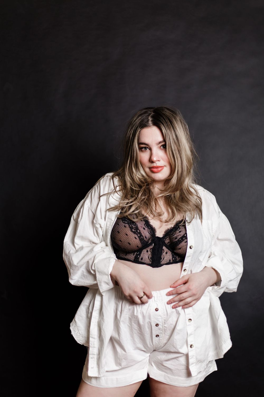 Intimate boudoir photo featuring black lace lingerie with white button-down shirt and shorts against dark background.