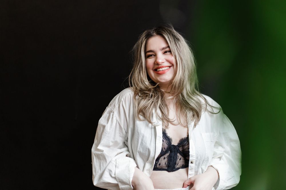Portrait against green backdrop wearing white oversized shirt and black undergarment.