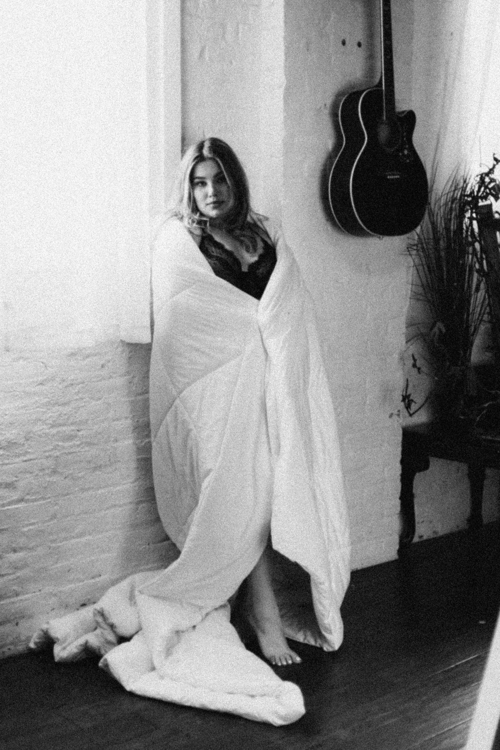 Black and white artistic photos of someone in flowing white fabric on floor with guitar hanging on wall.