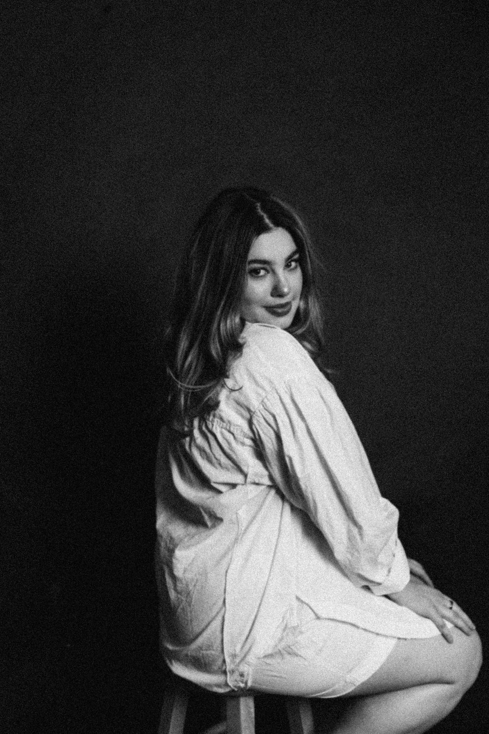 Black and white portrait of person in white shirt against dark background with dramatic lighting.