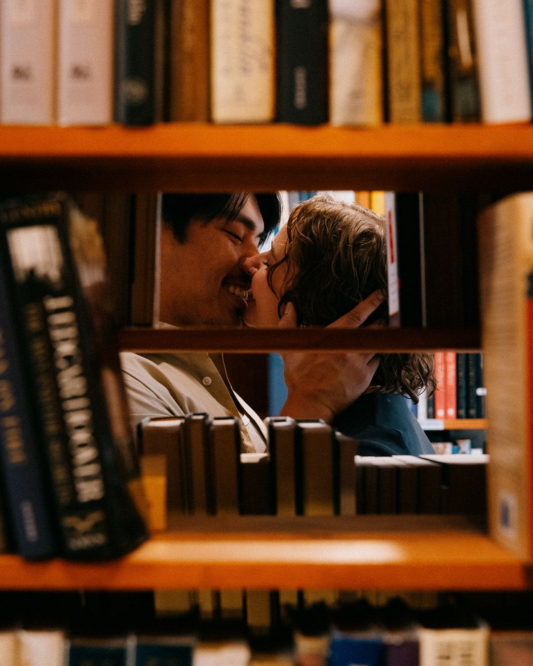 A couple kissing, as viewed through a bookshelf on the other side.