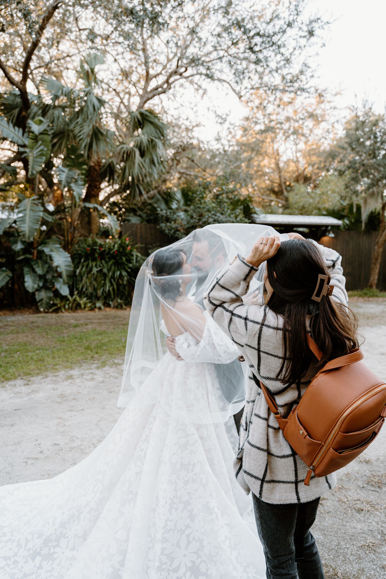 Photographer with camera and backpack capturing bride in her wedding dress.